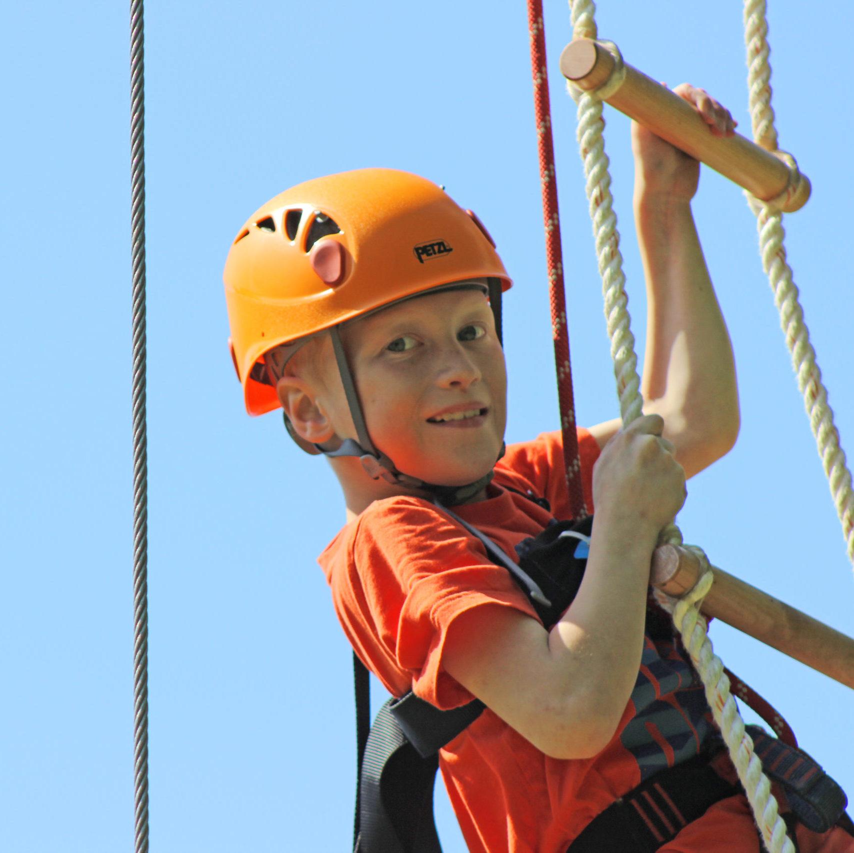 Young male camper smiling while climbing the rope ladder at Camp Kennebec
