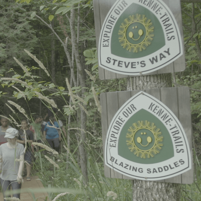 Two trail signs and a group of campers coming back from a hike at Camp Kennebec