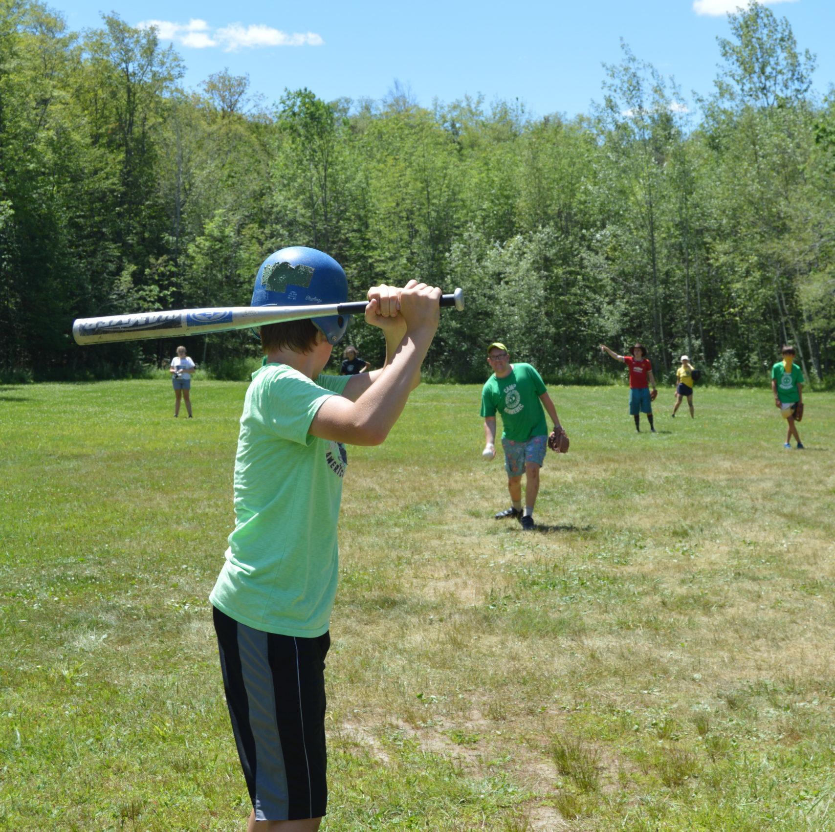 Male camper wearing a green tshirt holding baseball bat while playing baseball at Camp Kennebec
