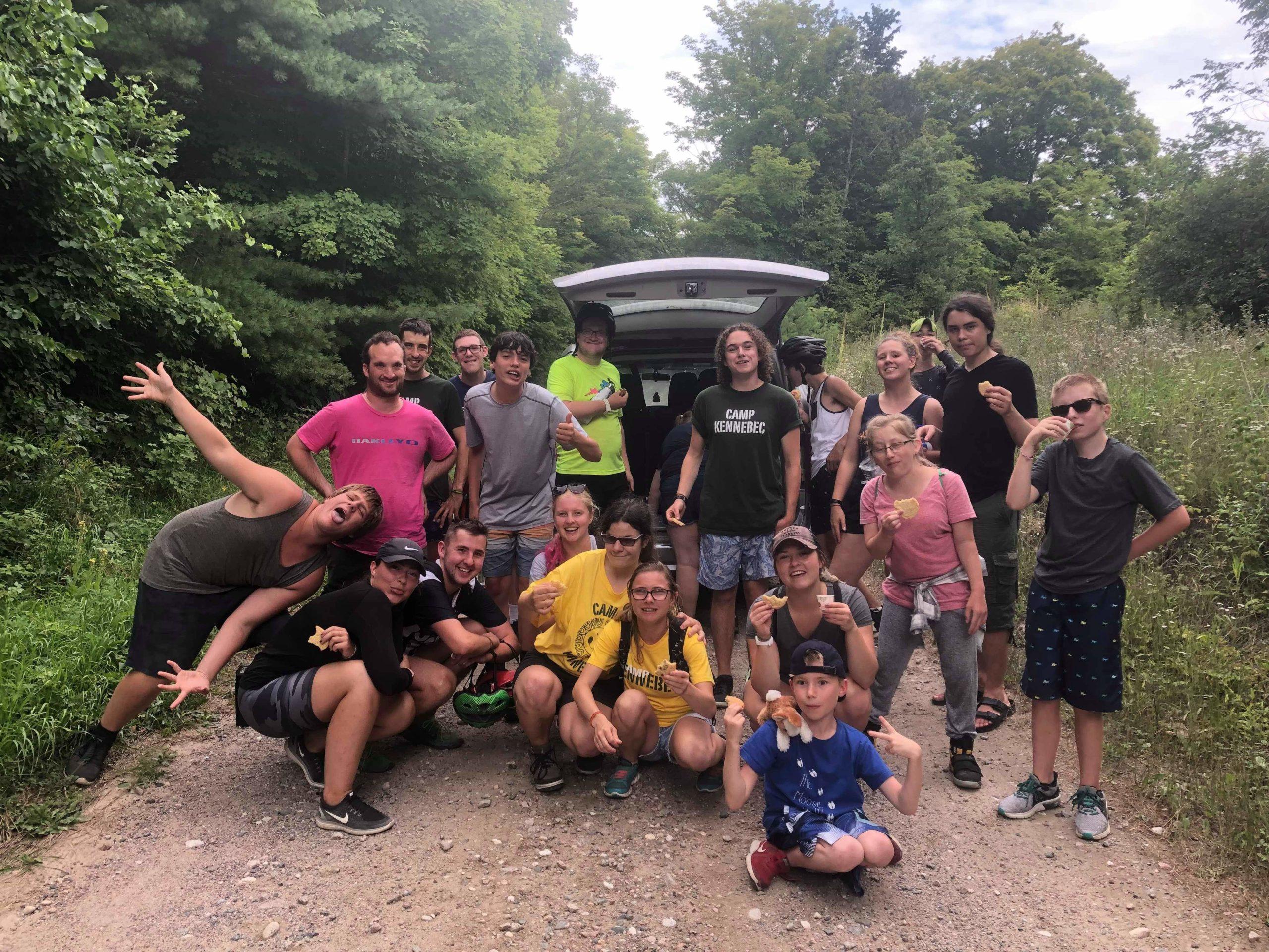 Group of campers heading out on a hike behind a van parked on Camp Kennebec's 4km dirt road drive way
